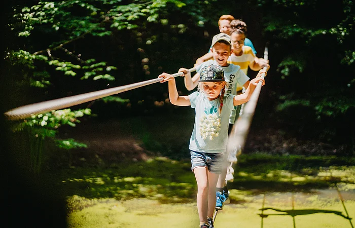 Eine Familie überquert einen Wassertümpel über dem Seilparcours