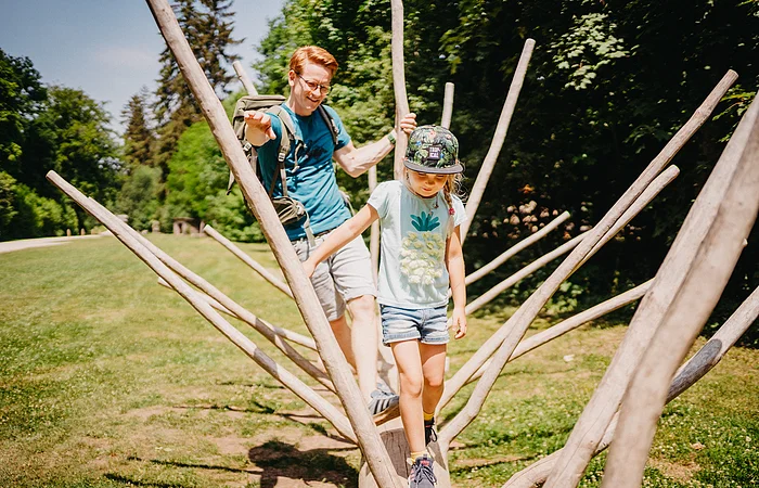 Vater und Tochter klettern durch einen Ästebaum auf einer grünen Waldlichtung im Walderlebniszentrum Schernfeld.