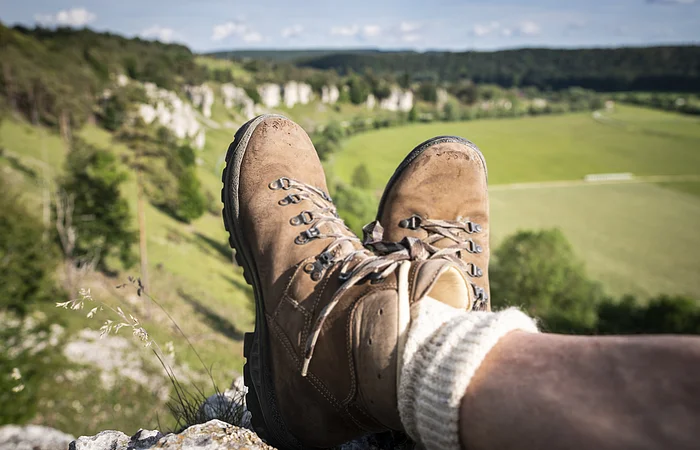 Braune Wanderschuhe mit hellen Socken sind im Mittelpunkt. Dahinter erstrecken sich die zwölf Apostel, die am Altmühltal-Panoramaweg liegen.