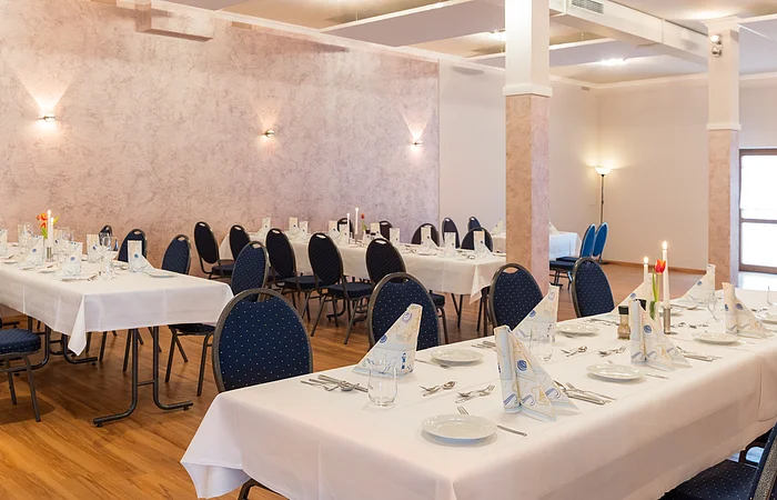 Tische mit weißer Tischdecke und Deko stehen im Raum mit dunkelblauen Stühlen.