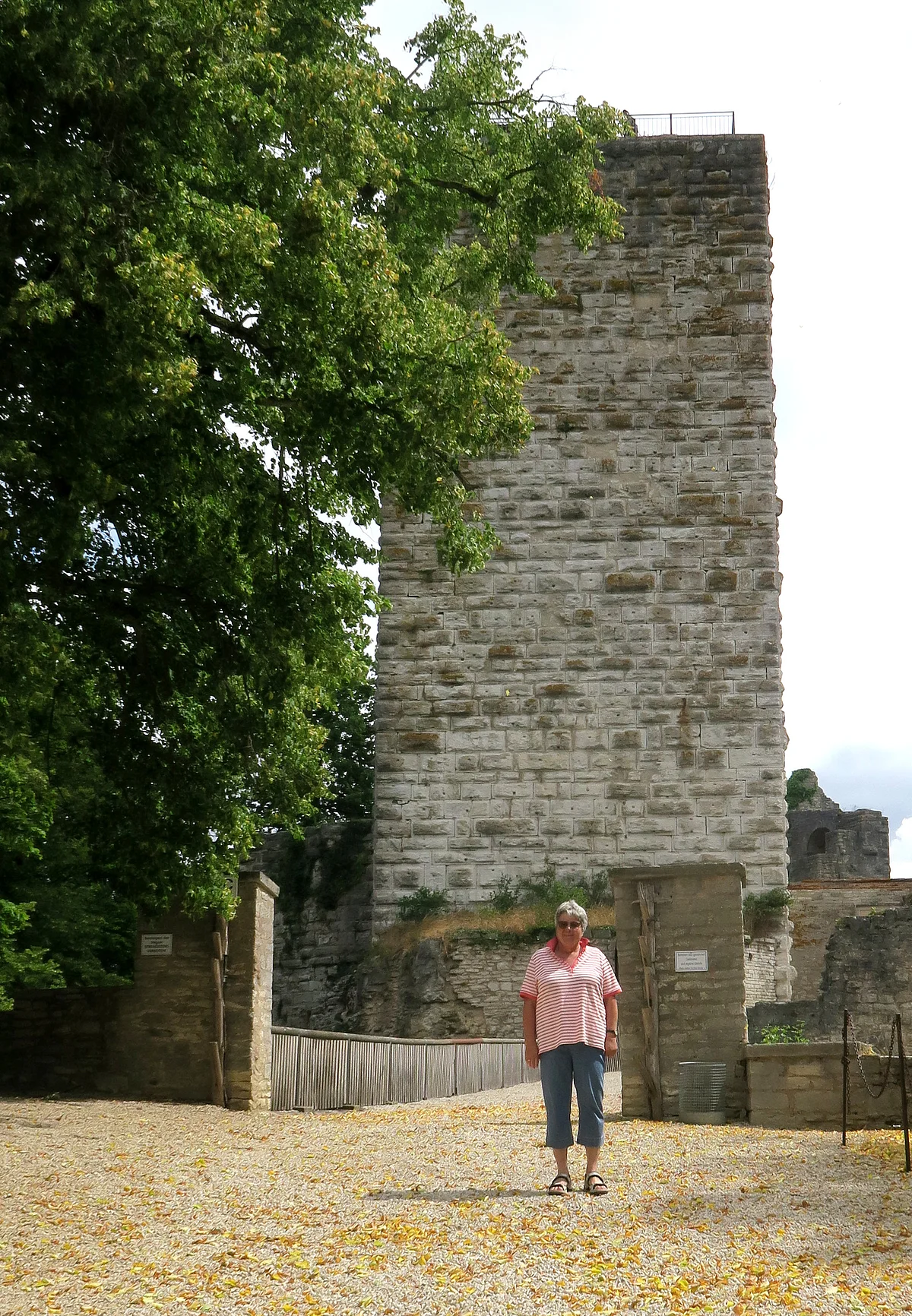 Frau in sommerlicher Kleidung steht vor Brücke, die auf einen Burgturm zuführt.