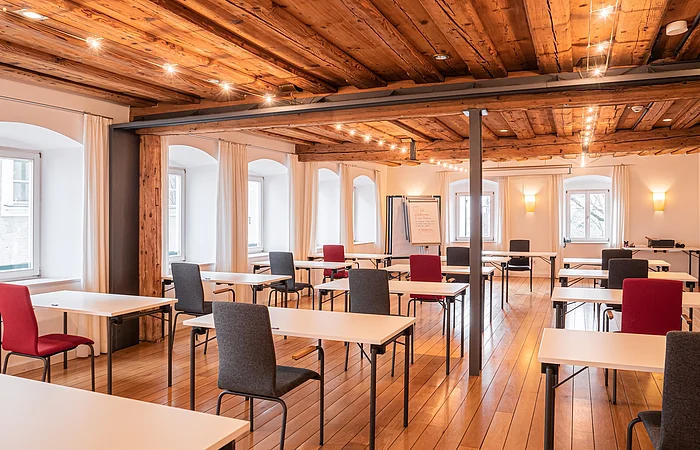 Die Einzeltische sind mit Blick nach vorne gerichtet platziert. Der Raum hat viele Holzelemente.