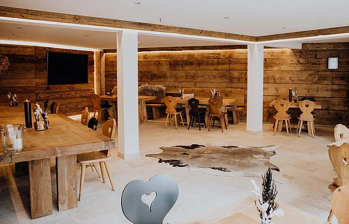 Die ländlich eingerichtete Stube ist möbliert mit massiven Holztischen, rustikalen Holzstühlen und einem Teppich aus Tierfell.