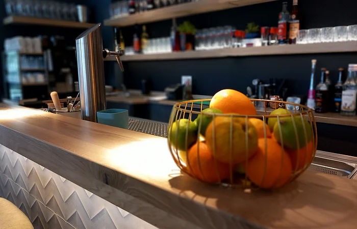 Die Bar ist aus Holz. Die Regale sind gut gefüllt mit leckeren Spirituosen und Gläsern. Auf dem Tresen steht ein Obstkorb als Dekoration.