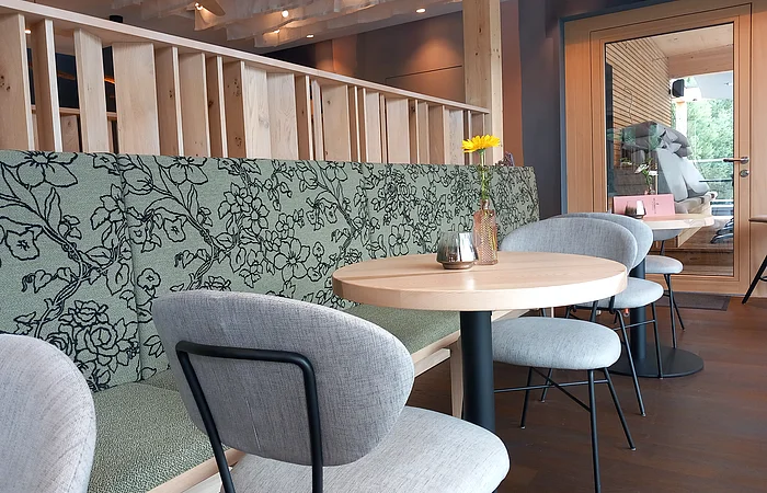 Der Essbereich ist modern mit Sitzbänken und Stühlen in hellen Stofftönen, sowie hellen Holztischen eingerichtet.