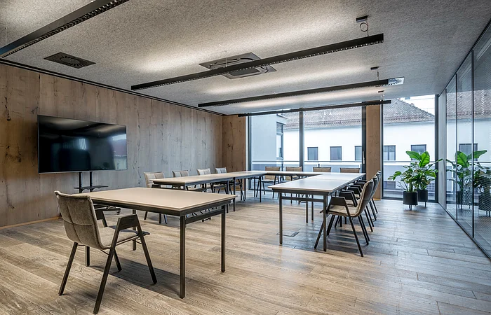 Die grauen Stühle sind um einen weißen langen Tisch ausgerichtet. Der Raum ist minimalistisch eingerichtet.