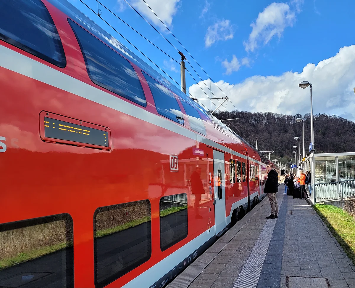 Eine Regionalbahn hat am Gleis gehalten und Reisende warten darauf, dass sich die Türen öffnen.