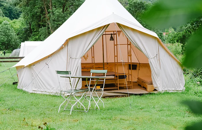 Ein Zelt ist aufgebaut auf einer grünen Wiese und vor dem Zelt stehen zwei Stühle mit einem Tisch.