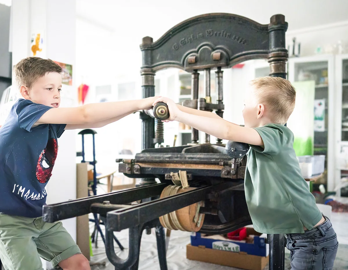 KunstMuseum Donau-Ries Zwei Jungs testen den Bilddruck mit einer händischen Maschine im KunstMuseum Donau-Ries.