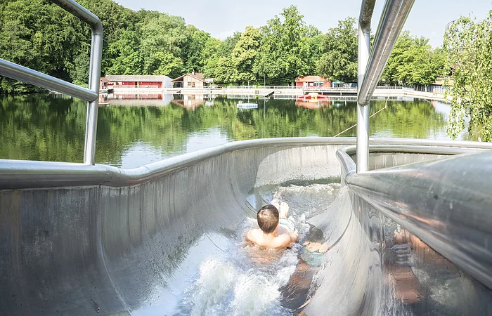 Ein Kind rutscht auf der Wasserrutsche am Waldsee herunter.