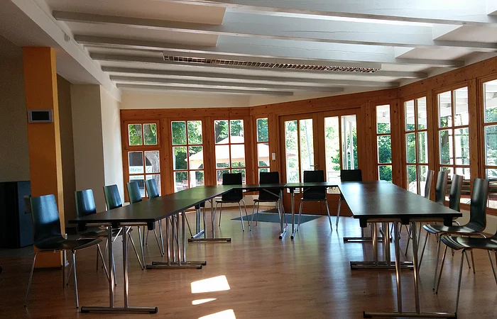 Die offenen Fenster im Hintergrund geben dem Raum natürliches Licht. Die schwarzen Stühle sind um einen Tisch in U-Form gestellt.