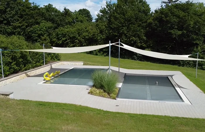 Rechteckiger Pool mit Abdeckung, umgeben von Rasen und Bäumen, mit Sonnensegeln und gelbem Schwimmtier.