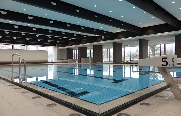 Das Monheimer Hallenbad, das Jurabad, mit gefülltem Schwimmbecken, Startblöcken und großen Fenstern, die Tageslicht hereinlassen.