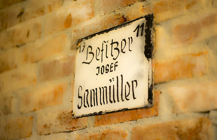 Die Steinwand ist mit einem Schild "Sammüller" geschmückt.