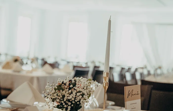 Blick auf einen in hellen Farben gedeckten Tisch mit Gläsern, Blumenvase und Kerze.