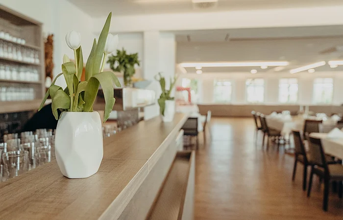 links sieht man die Theke mit Gläser und Dekoration. Rechts sieht man Tische und Stühle.