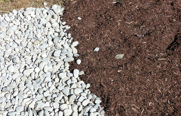 Weiße Kieselsteine grenzen an eine Fläche mit braunem Mulch.