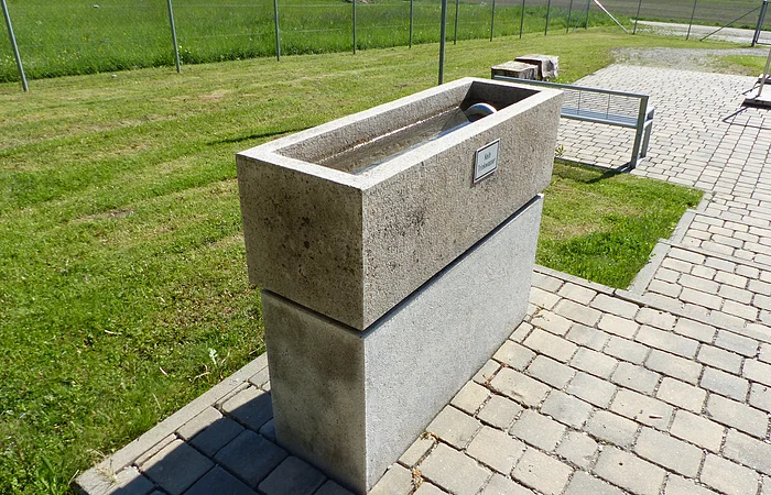 Armbecken der Kneipp Gesundheitsanlage in Monheim auf gepflastertem Weg neben einer Wiese, mit einem Wasserhahn an der Oberseite.