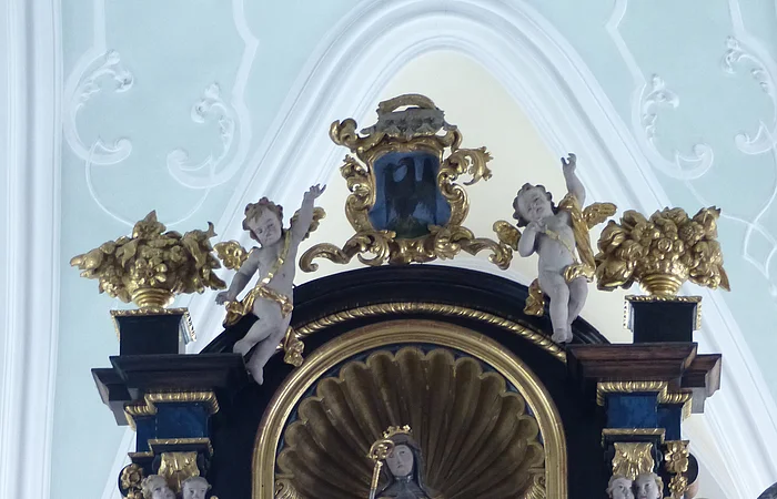 Barockes Altarretabel mit goldener Skulptur und Putten, verziert mit floralen Elementen und Engelsköpfen.
