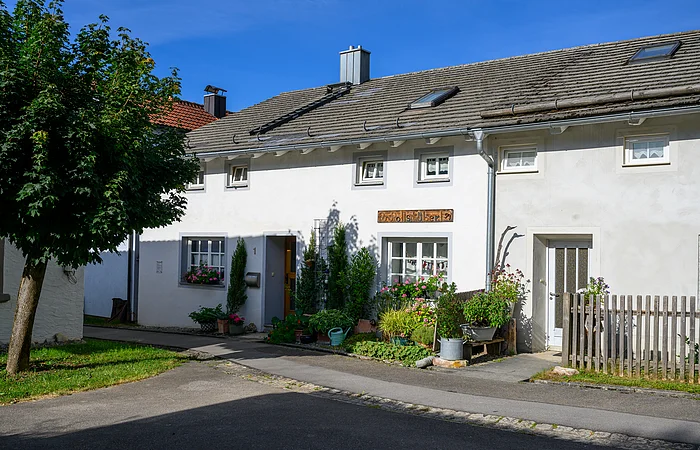 Ein Jurahaus in Suffersheim, das Wollstüberl. vor dem Haus befinden sich einige Stäucher, Die Tür und die Fenster sind mit einem hellgrauen Farbanstrich abgesetzt