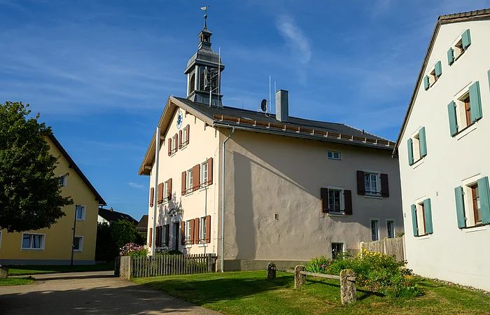 Zwei Gebäude mit Fensterläden und einem Turm, umgeben von einem Garten und einem Baum.