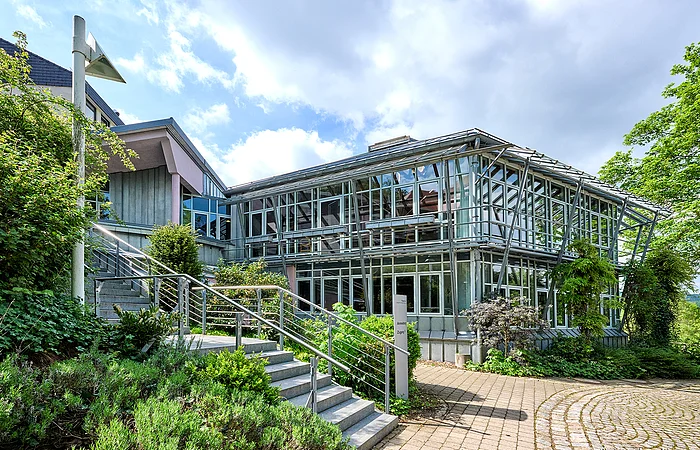 Das EBZ von außen mitten im Sommer umringt von grünen Bäumen und blauem Himmel.