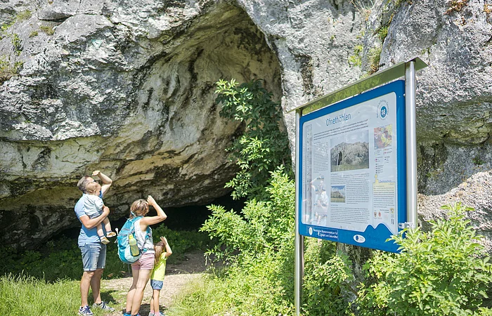 Eine Familie steht vor einer Höhle, daneben ein Informationsschild mit der Aufschrift "Ofnethöhlen".