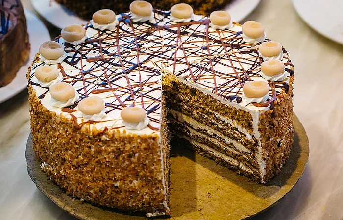 Eine mehrschichtige Torte mit Sahne, Schokoladendekor und Marzipanverzierung auf einem Tisch. Ein Stück fehlt.