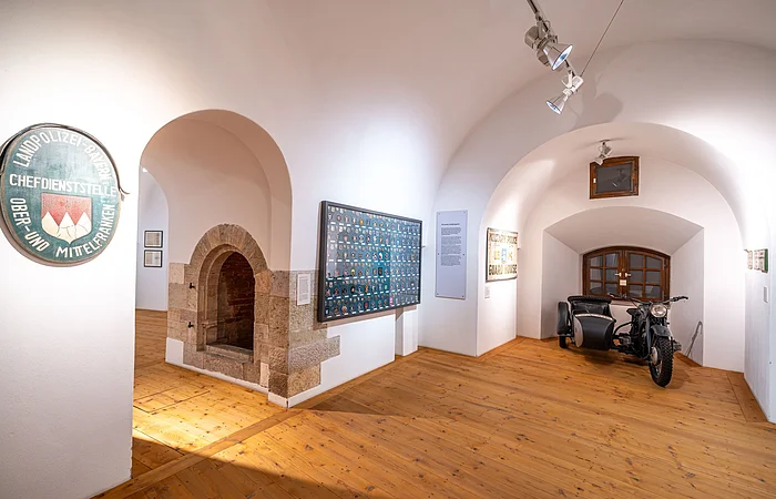 Museumsausstellung mit Polizeischildern, einem Motorrad mit Beiwagen und einem steinernen Torbogen.