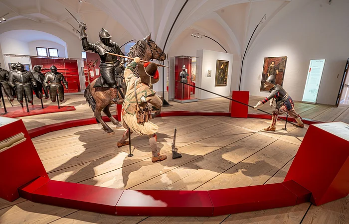Ausstellung mit mittelalterlichen Rüstungen und Figuren in Kampfpose in einem Museum.