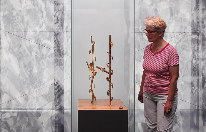 Eine Person betrachtet eine Skulptur mit goldfarbenen Zweigen und Blättern in einer gläsernen Vitrine.