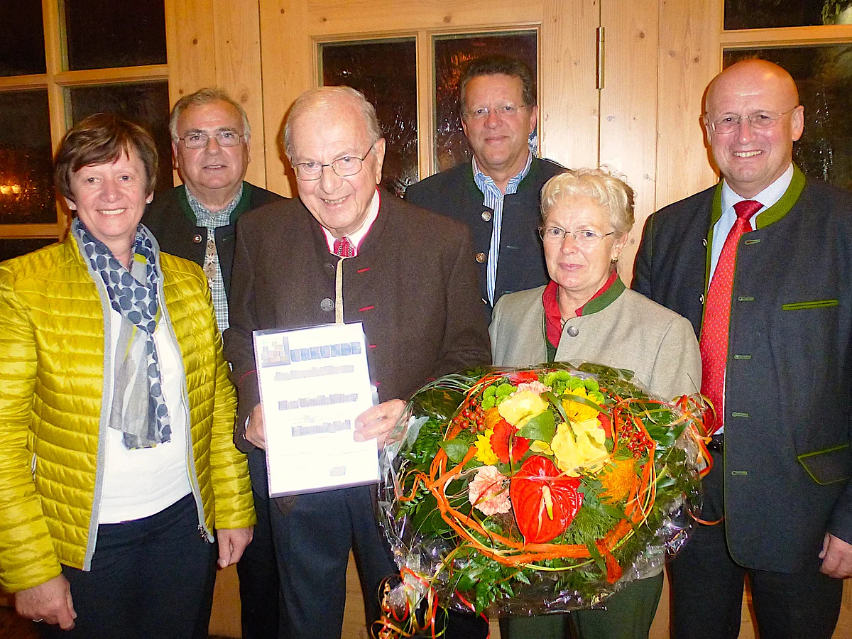 Sechs Personen stehen zusammen, eine Person hält eine Urkunde, eine andere einen Blumenstrauß.