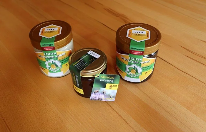 Drei Honiggläser mit Etiketten "Echter Deutscher Honig" auf einem Holztisch.
