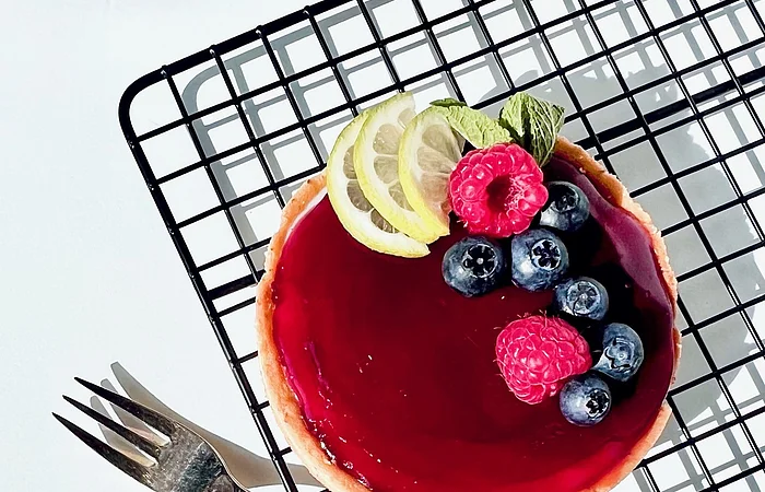 Ein kleiner Kuchen mit roter Glasur, garniert mit Beeren und Zitronenscheiben, auf einem Gitterrost.