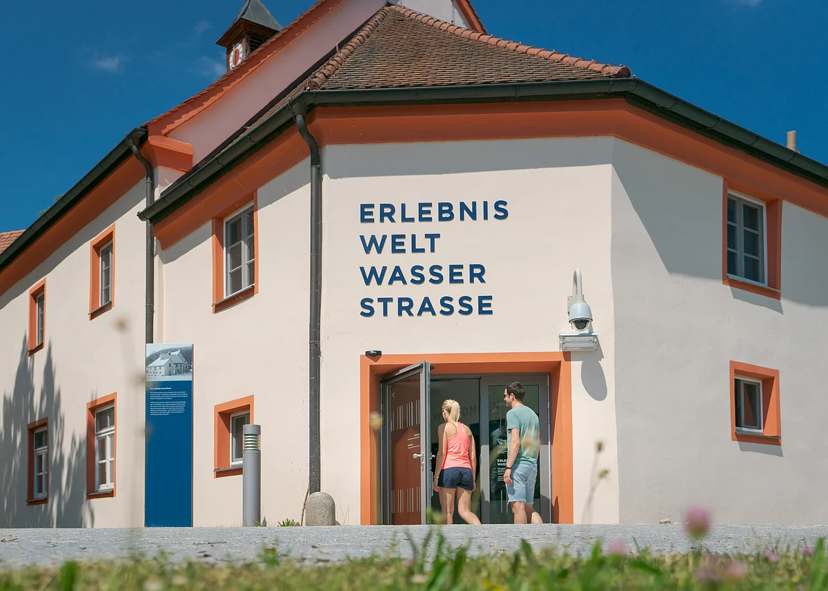 Erlebniswelt Wasserstraße in Beilngries Gebäude mit der Aufschrift "ERLEBNIS WELT WASSER STRASSE", zwei Personen betreten es.
