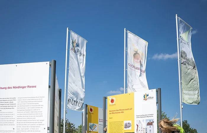 Ein Kind und eine Frau betrachten Informationstafeln im Freien, umgeben von Fahnen.