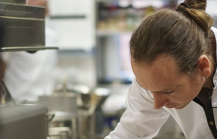 Ein Koch in einer Küche verfeinert ein Fischgericht auf einem Teller mit einer Soße.