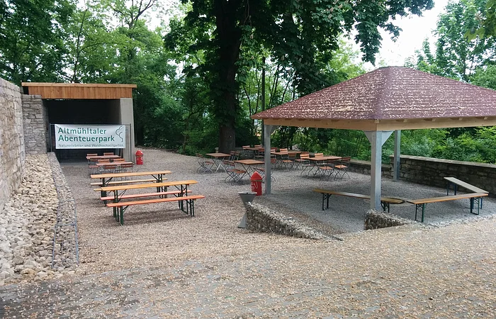 Außenbereich mit Bierzeltgarnituren, Pavillon und Schild "Altmühltaler Abenteuerpark". Bäume im Hintergrund.