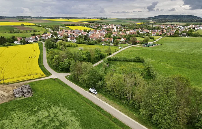Luftaufnahme einer ländlichen Landschaft mit Feldern, einem Dorf und einem Wohnmobil auf einer Straße.