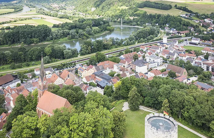 Luftaufnahme einer Stadt mit Kirche, Turm und Fluss in einer grünen Landschaft.