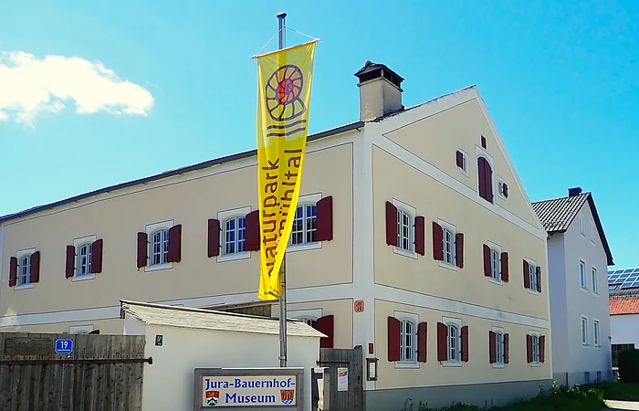 Gebäude mit gelber Flagge "Naturpark Altmühltal" und Schild "Jura-Bauernhof-Museum" davor.