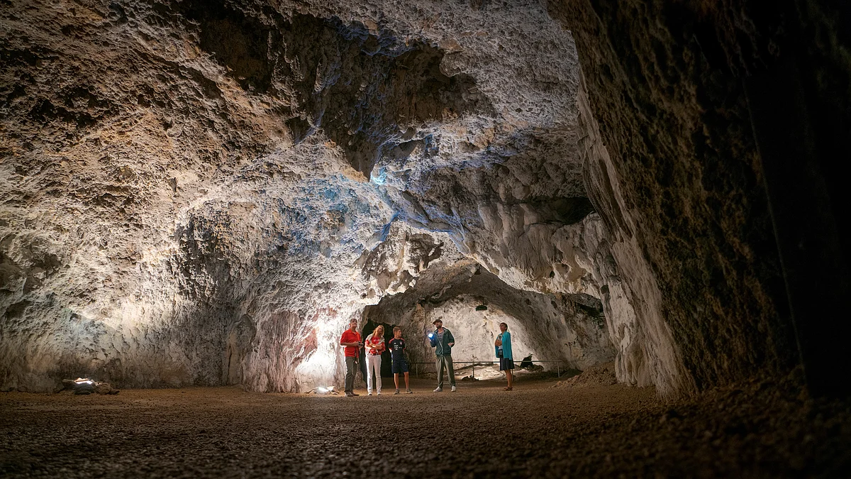 Fünf Personen stehen in einer großen, beleuchteten Höhle mit unregelmäßigen Felswänden und Boden aus Erde.
