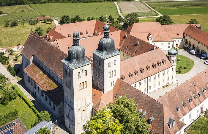 Luftaufnahme eines historischen Gebäudekomplexes mit zwei Kirchtürmen und roten Ziegeldächern in ländlicher Umgebung.