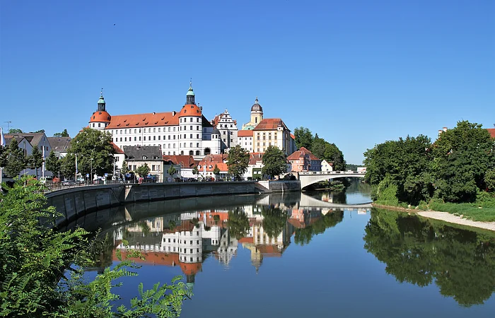 Stadtansicht mit Schloss und Brücke, Spiegelung im Fluss, blauer Himmel, Bäume am Ufer