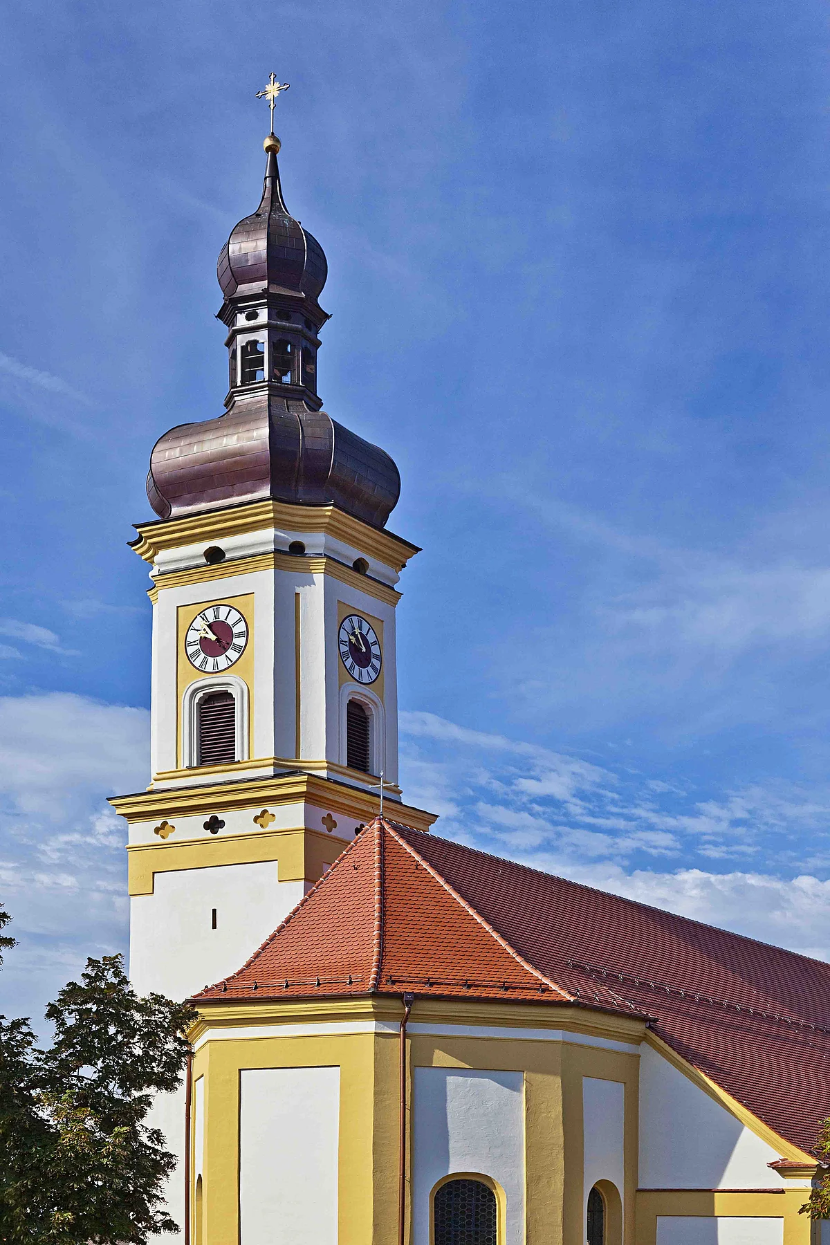 Kirchturm mit Zwiebelhaube und Uhr an gelb-weißer Kirche unter blauem Himmel.