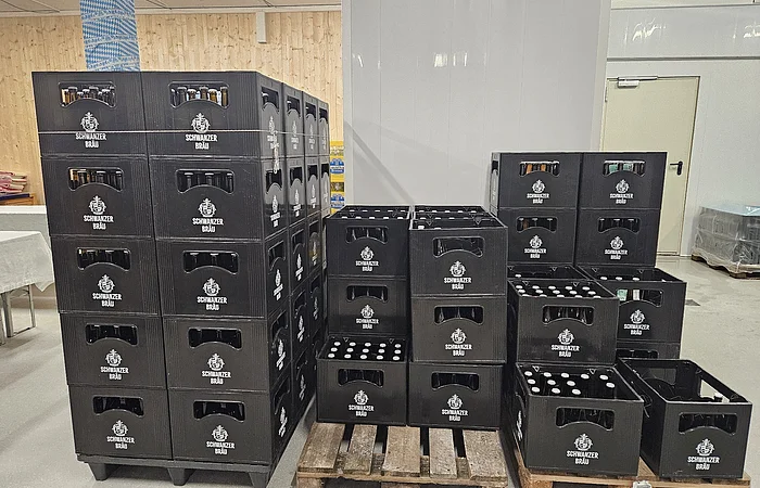 Schwarze Getränkekisten mit Flaschen der Marke Schwarzer Bräu gestapelt auf Paletten in einem Lagerraum.