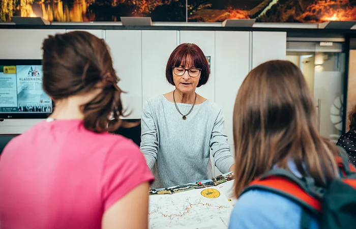 Frau zeigt zwei Personen eine Landkarte in einem Informationsbüro.