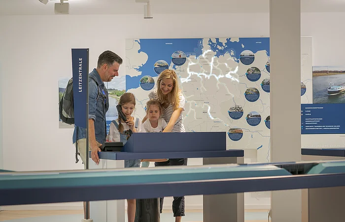 Familie mit zwei Kindern steht an interaktivem Ausstellungstisch vor beleuchteter Deutschlandkarte im Museum.