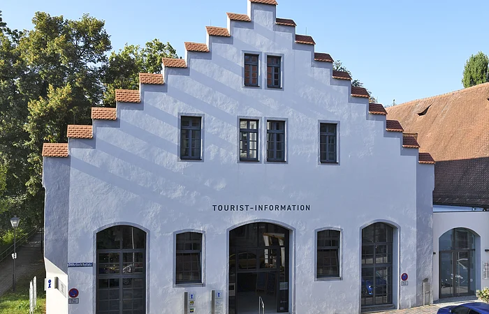 Gebäude mit Treppengiebel und Schriftzug Tourist-Information, davor gepflasterte Straße und blauer Pkw.