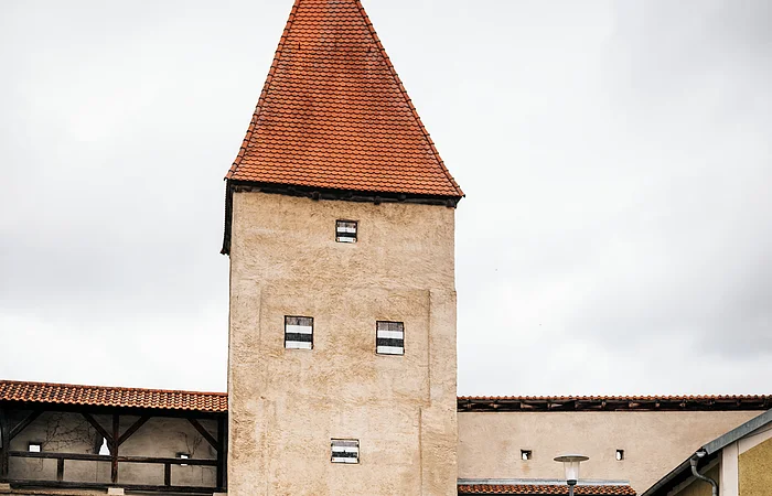 Zwei Radfahrer fahren an einem historischen Stadttor mit rotem Dach und Durchfahrt vorbei.
